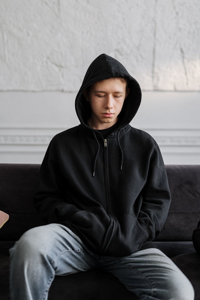 Man in Black Hoodie Sitting on Brown Couch