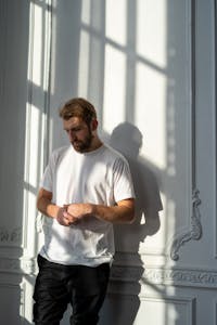 Man in White Crew Neck T-shirt Standing Beside Window