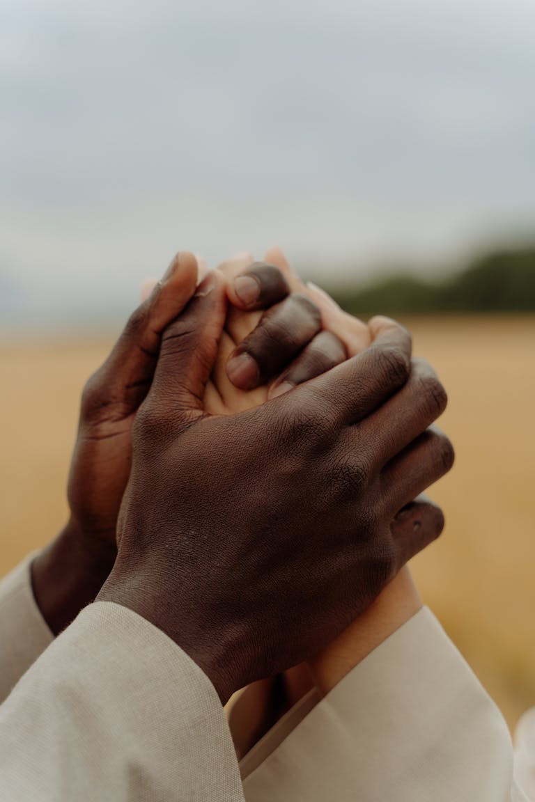 A close-up of two people of different ethnicities holding hands outdoors, symbolizing unity and support.