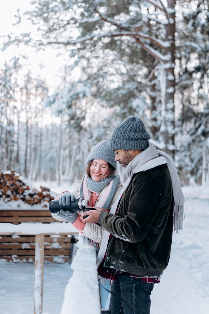 A happy couple in winter clothing, enjoying hot drinks outdoors during a snowy day.