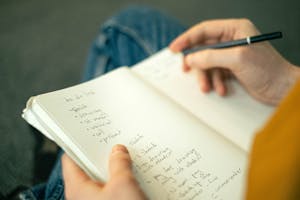 Close-up of a person taking notes in a notebook, writing a to-do list with a pencil.