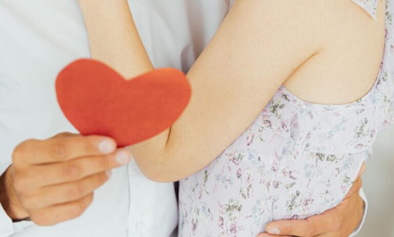 A loving couple embraces while holding a heart-shaped cutout, creating a warm and affectionate scene.