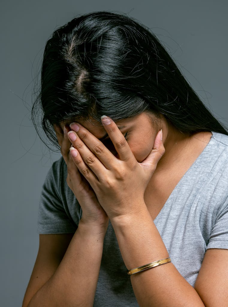 A woman hides her face in hands showing deep emotion and sadness in a studio setting.