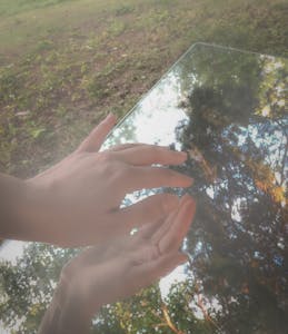 Hands touching a glass surface outdoors with trees reflecting, creating a serene ambiance.