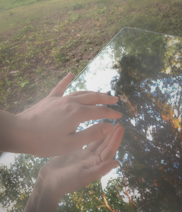 Hands touching a glass surface outdoors with trees reflecting, creating a serene ambiance.