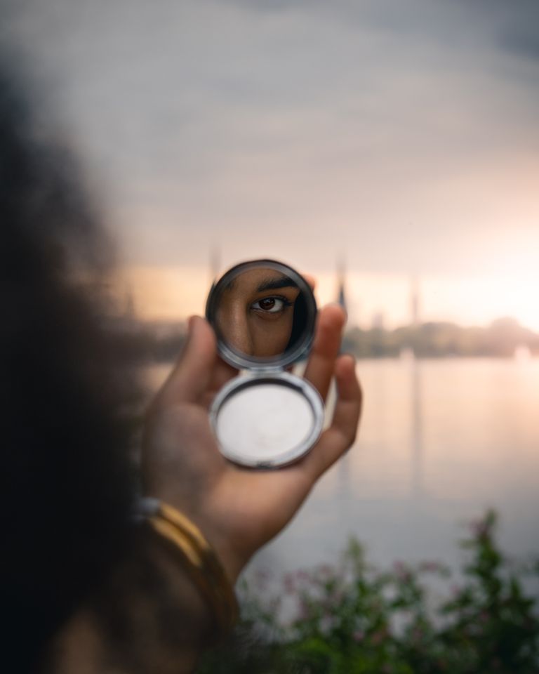 A captivating shot focusing on a reflection of an eye in a round mirror with Hamburg skyline in the background.