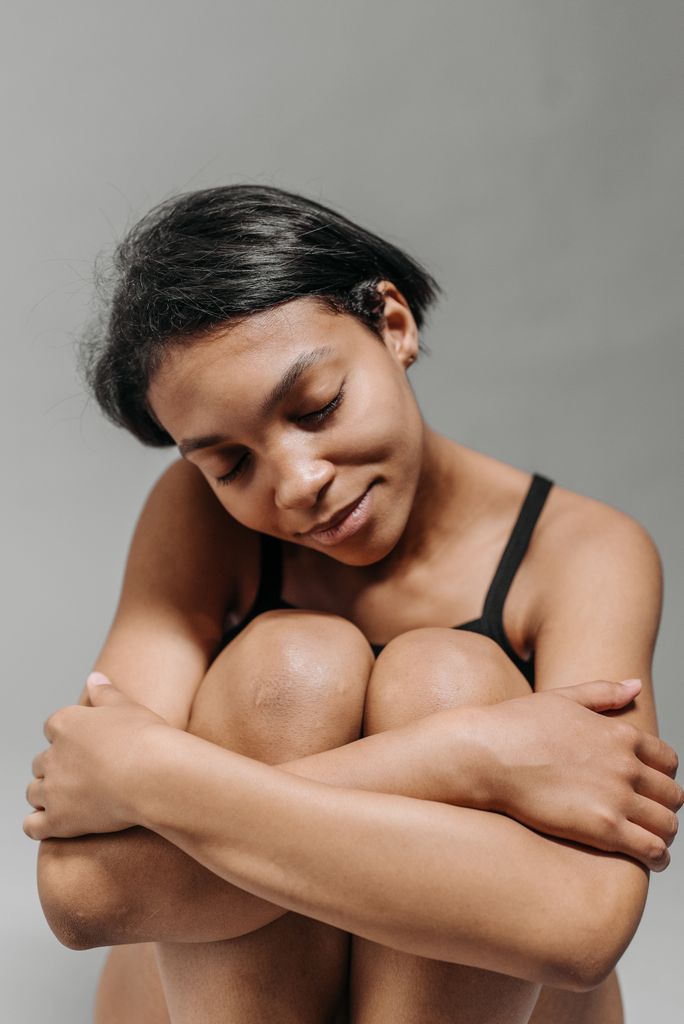 A peaceful young woman sits with eyes closed, embracing herself in a moment of introspection.