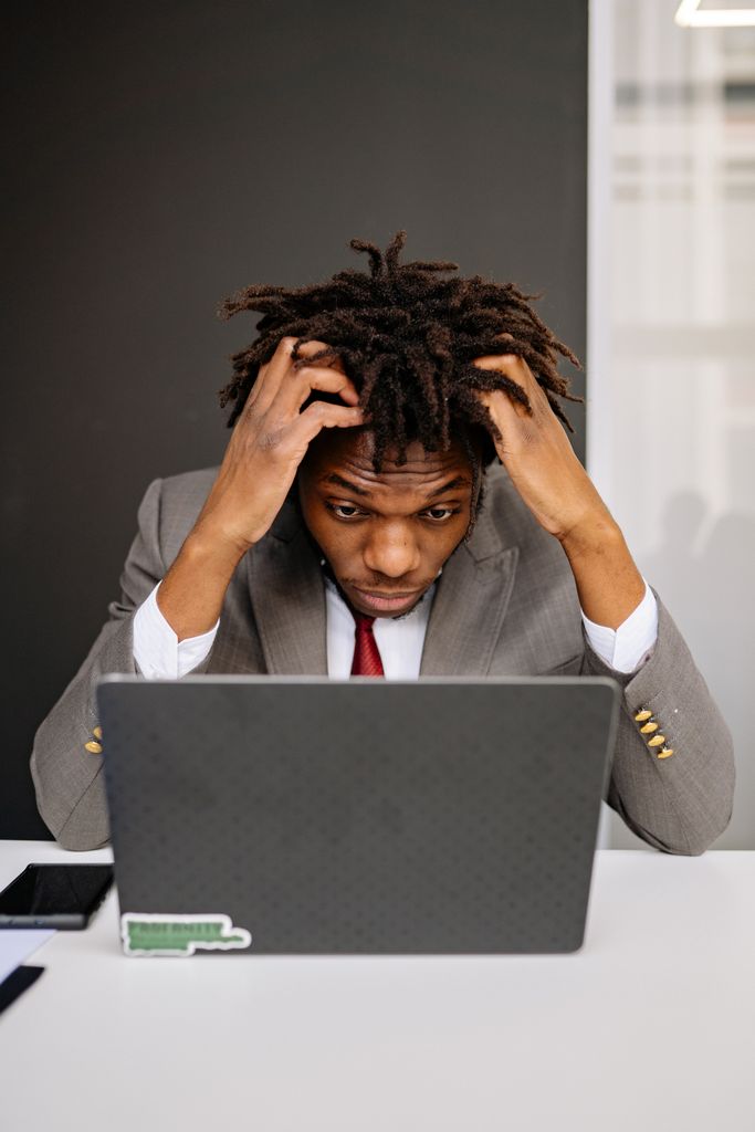 An exhausted businessman in a suit struggling with burnout while using a laptop.
