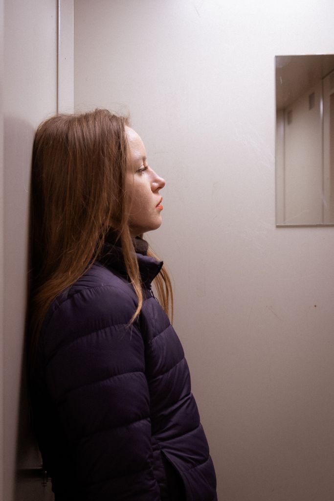 Side profile of an adult woman in a jacket leaning against a wall. Self-criticism.