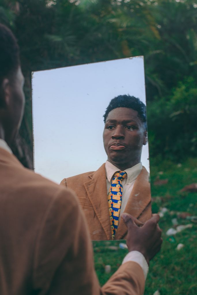 Man in a suit holding a mirror, reflecting in a garden setting in Accra, Ghana. Self-knowing